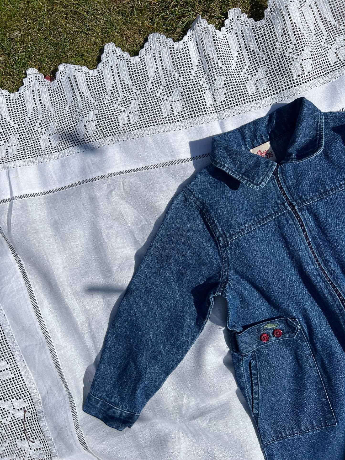 Close-up of a kids zip-up denim boiler suit featuring embroidered cherry details on organic vintage wash fabric, designed for girls aged 1-5 years.